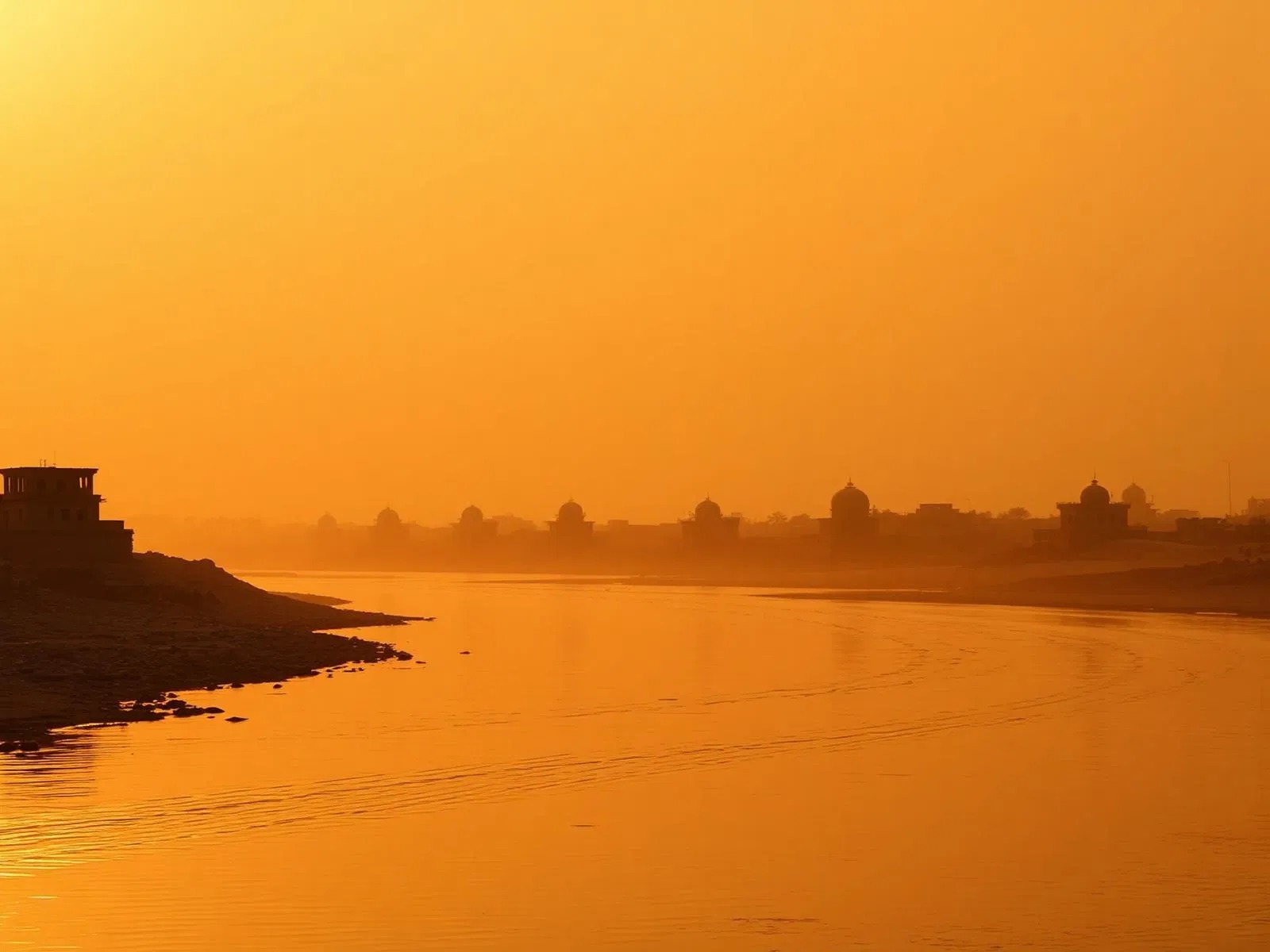 Sunset over a river with silhouettes of buildings